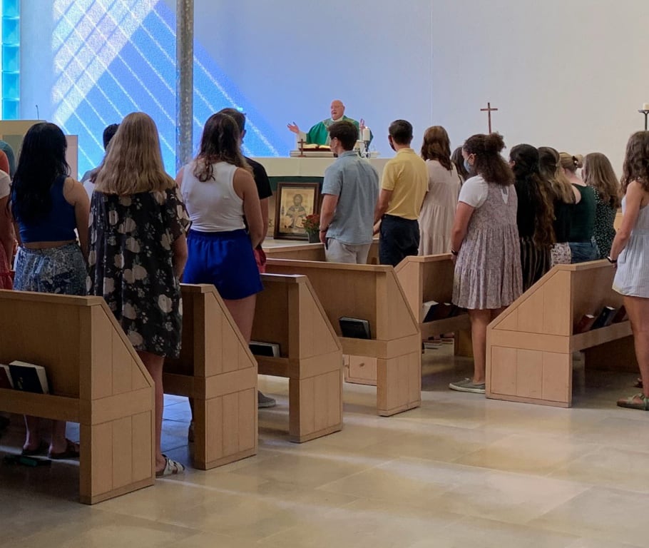 A group of people standing in a church pew, sharing heartfelt testimonials as they face the priest at the altar.