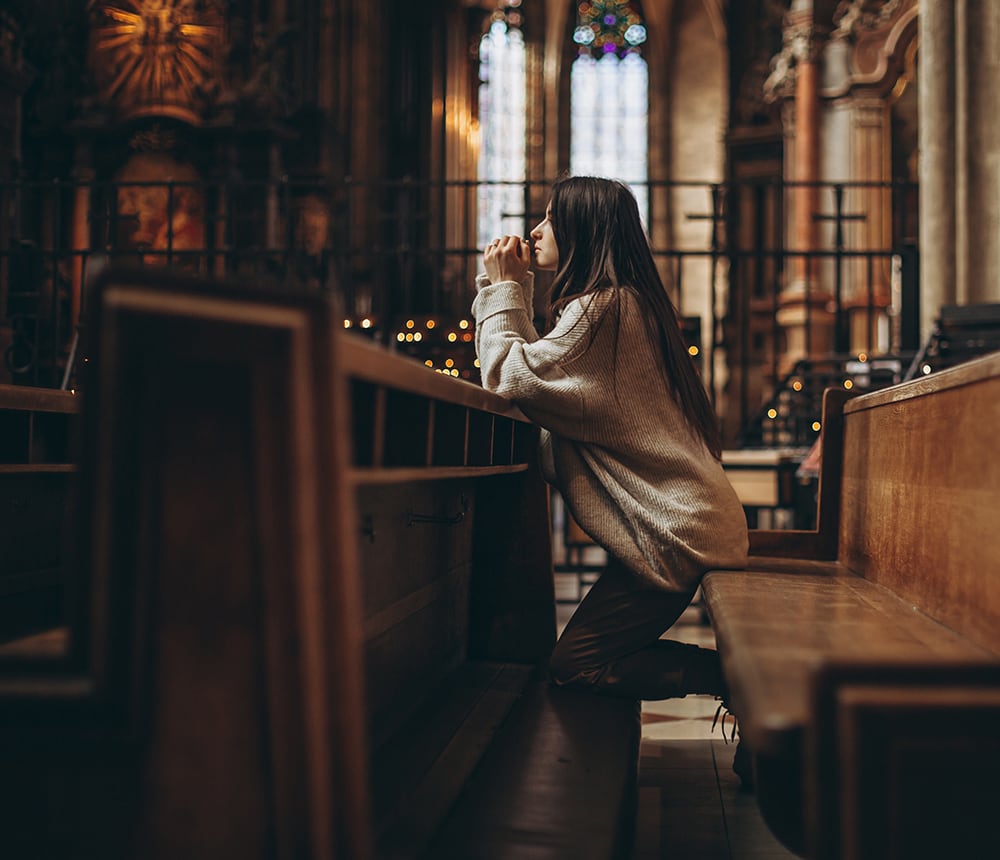 Kneeling in reflective prayer at a church pew, surrounded by dim lighting and ornate architecture, the ambiance quietly endorsed a sense of tranquility and reverence.