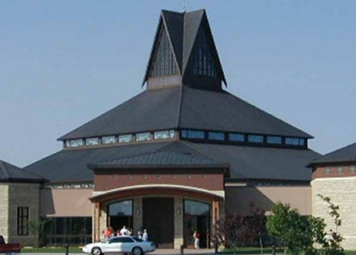 A modern building with a distinctive peaked roof stands proudly, as a small group of people gather near the entrance, sharing glowing testimonials about their experiences within.