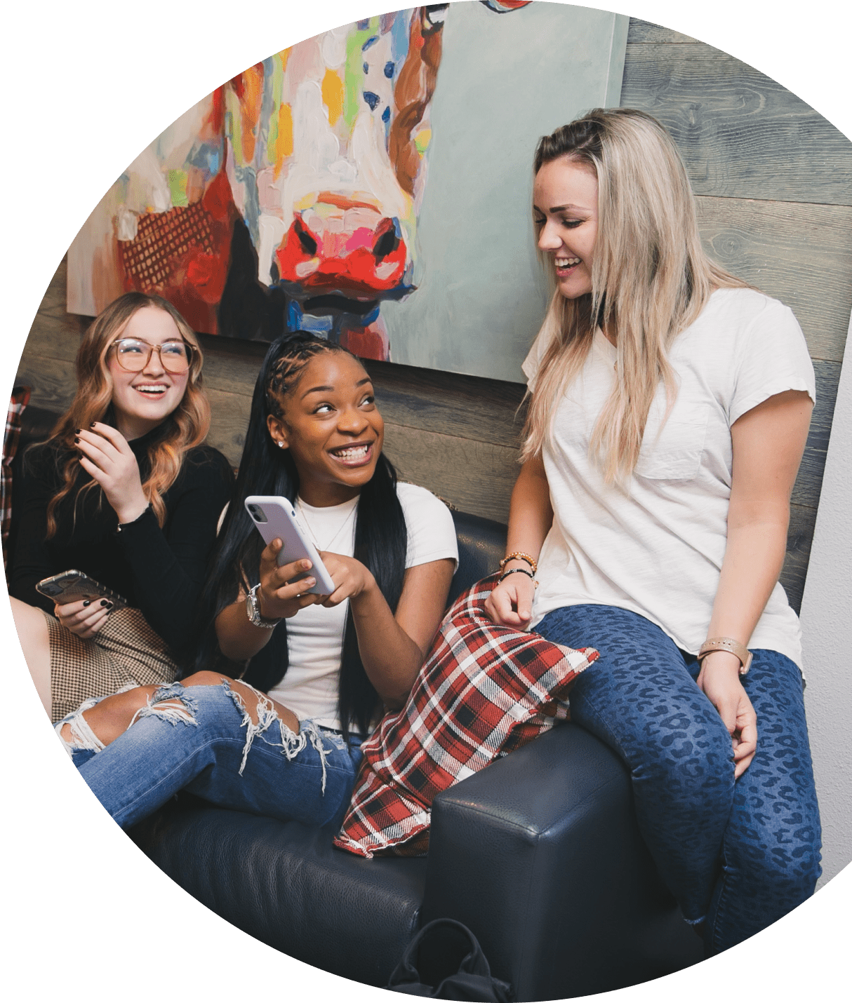 Three friends, laughing and chatting on a couch, share the warmth of the moment with colorful artwork in the background—a scene that reminds them to donate their laughter where it's needed most.